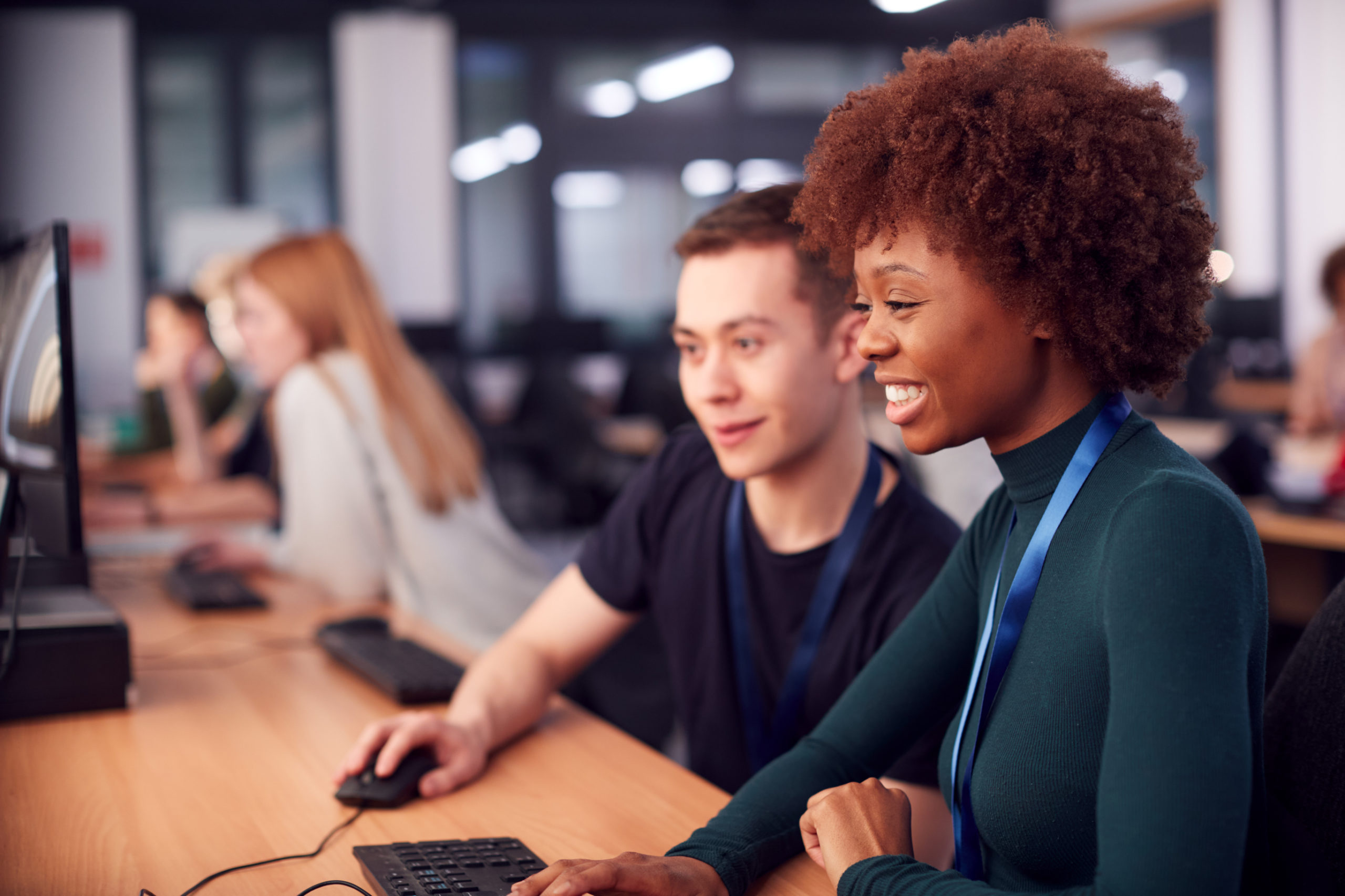 Group Of College Students Studying Computer Design Sitting At Line Of Monitors In Classroom