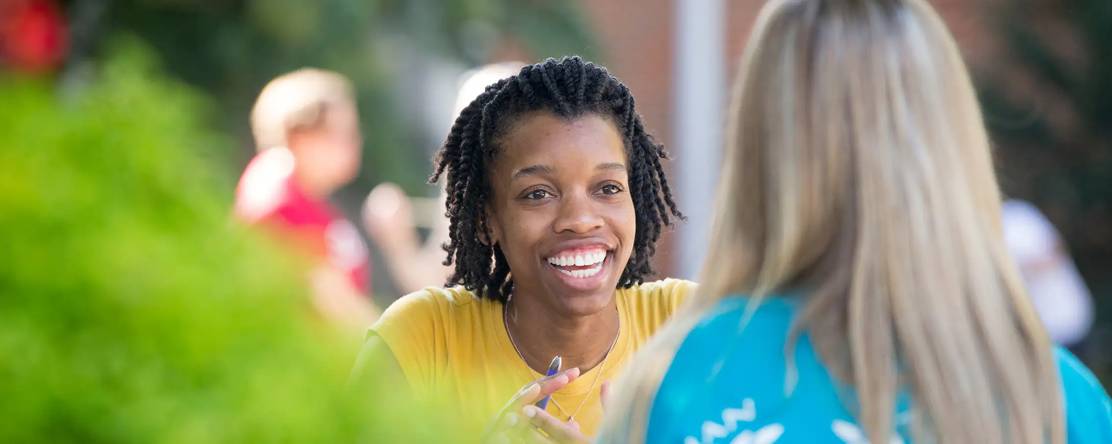 Two female students sit at an outdoor table smiling while talking