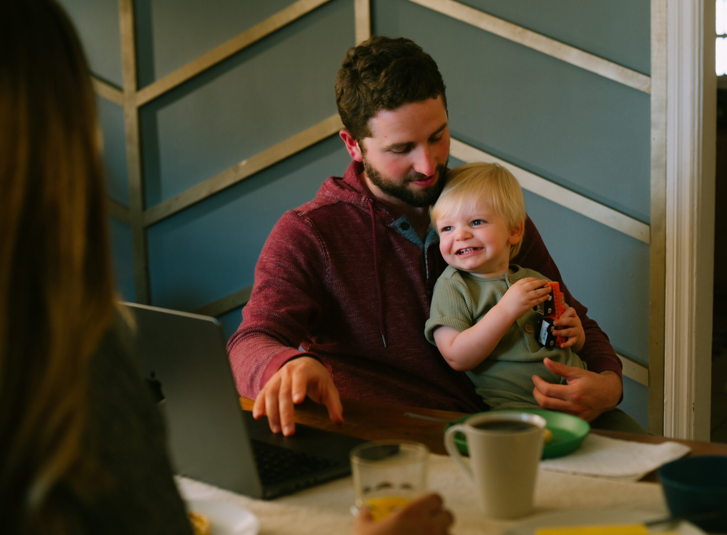 Father completes work on laptop with toddler in lap