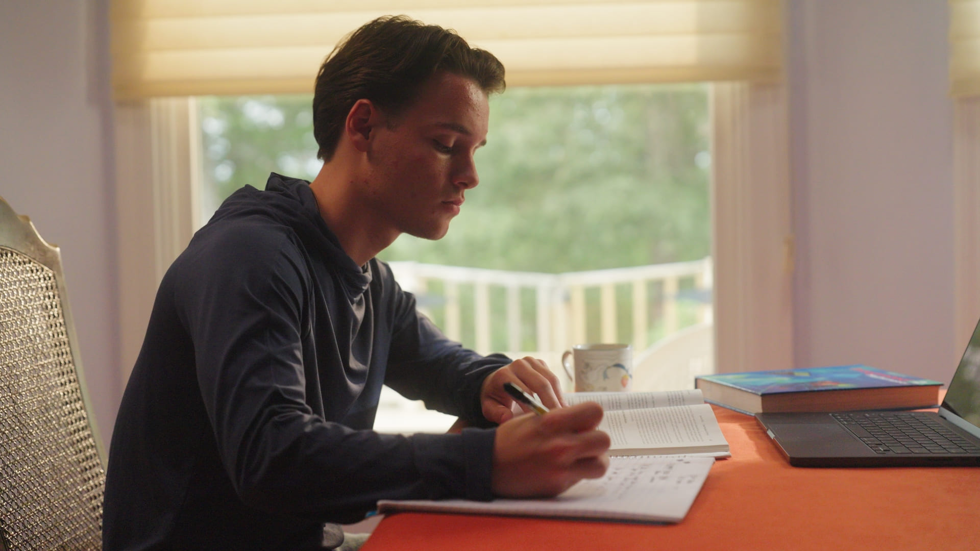 Student writing notes at desk near window